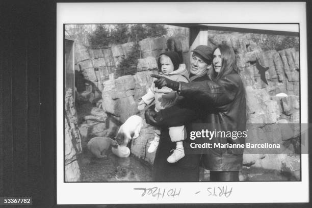 Artist Jenny Holzer standing behind her husband with child and pointing with her gloved hand; two polar bears play in water behind them at the...