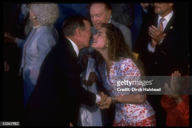 President Bush moving to kiss Brooke Shields, with Bob Hope among cast during taping of USO 50th anniv. TV special "Welcome Home America".