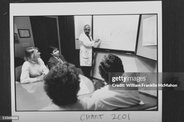 Neurologist Dr. Joel Saper founder of MI Head Pain Institute, pointing to drawing of human brain on blackboard as he instructs four of his staff...