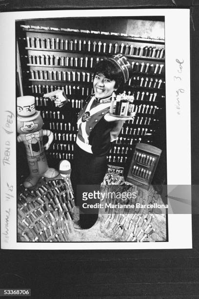 Pezhead collector Sue Sternfeld in Pez suit she made herself holding a plastic gun & tray filled with Pezheads in her Pezhead crowded living room.