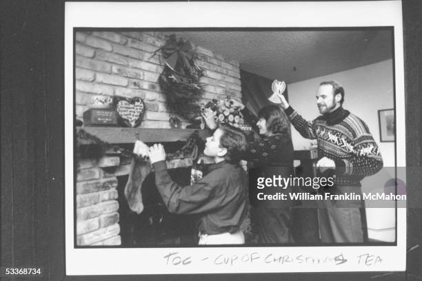 Author Tom Hegg holding up angel with wife Peggy & son Adam decorating their mantle with Christmas decorations at their home.