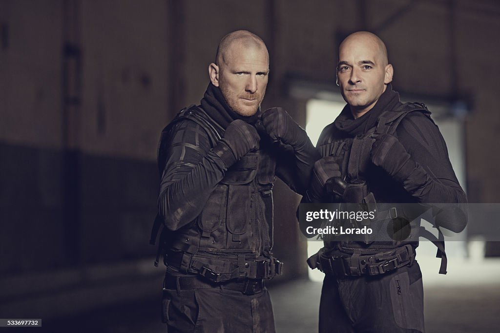 Two shaven headed swat team members posing in abandoned warehouse