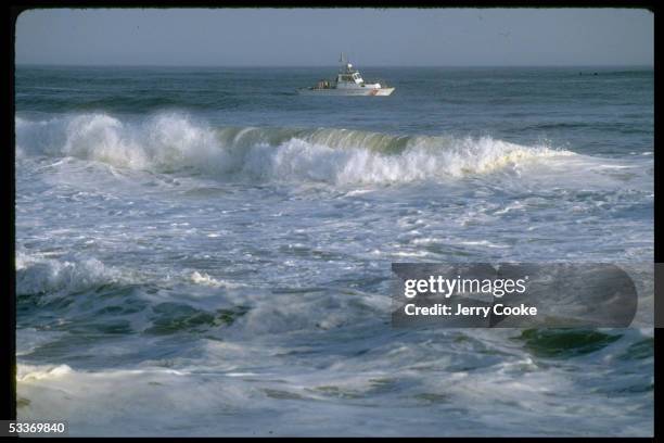 Excellent of waves rolling to shore of unidentified beach with Coast Guard cutter passing in distance.