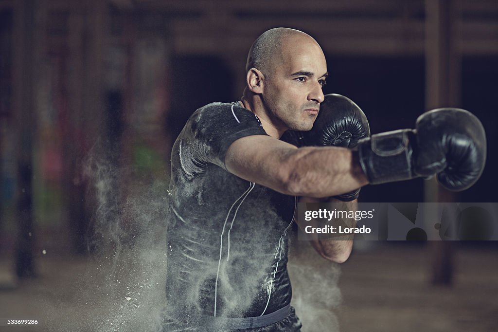 Shaven headed male athletic boxer training in abandoned warehouse