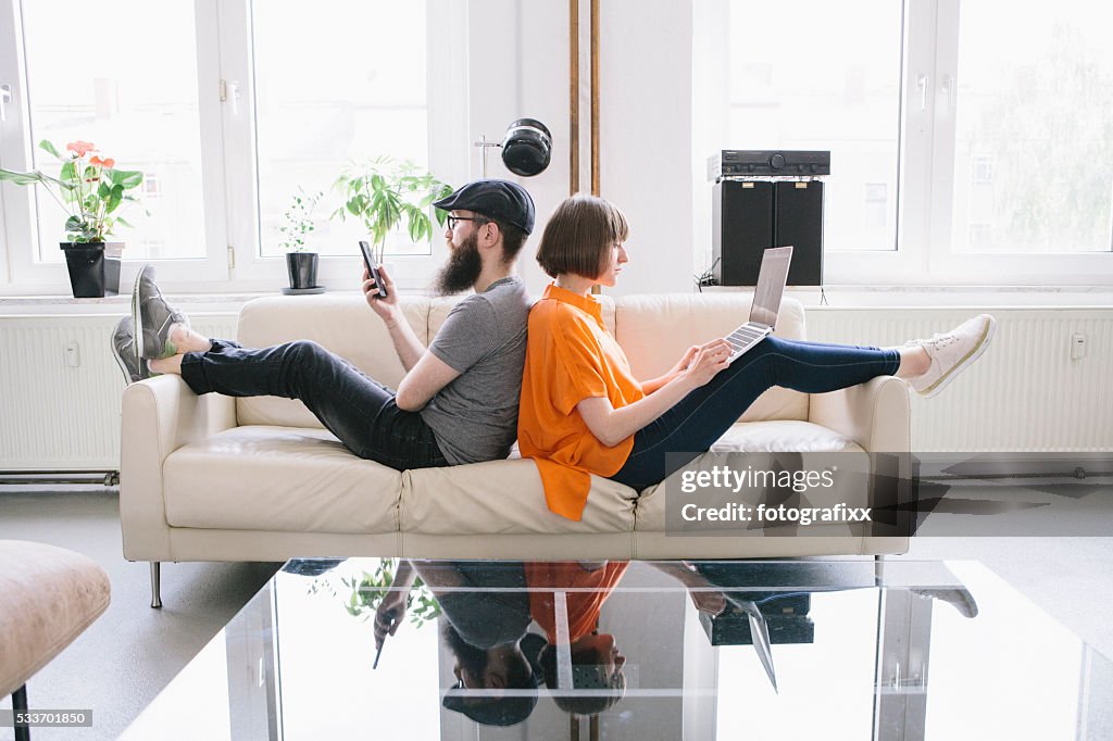 Hipster couple sit on couch and look into digital devices