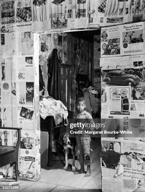 African-American child of sharecropper family & his dog standing in doorway of shack wallpapered with pages from magazines, East Feliciana Parrish. .