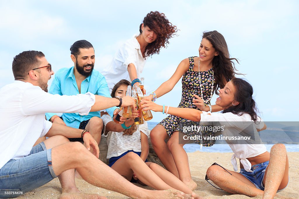 Grupo de amigos sentado sobre la arena y celebrar