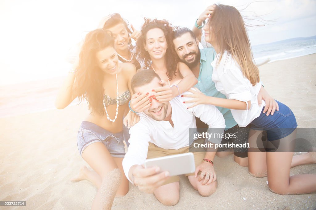 Cheerful friends making selfe on sand