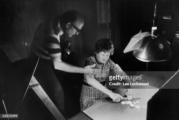 Chef Julia Child chopping squash as her husband, Paul photographs her for an upcoming cookbook.