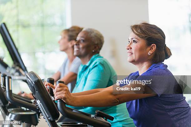 multiracial women riding exercise bikes at gym - aerobic stockfoto's en -beelden