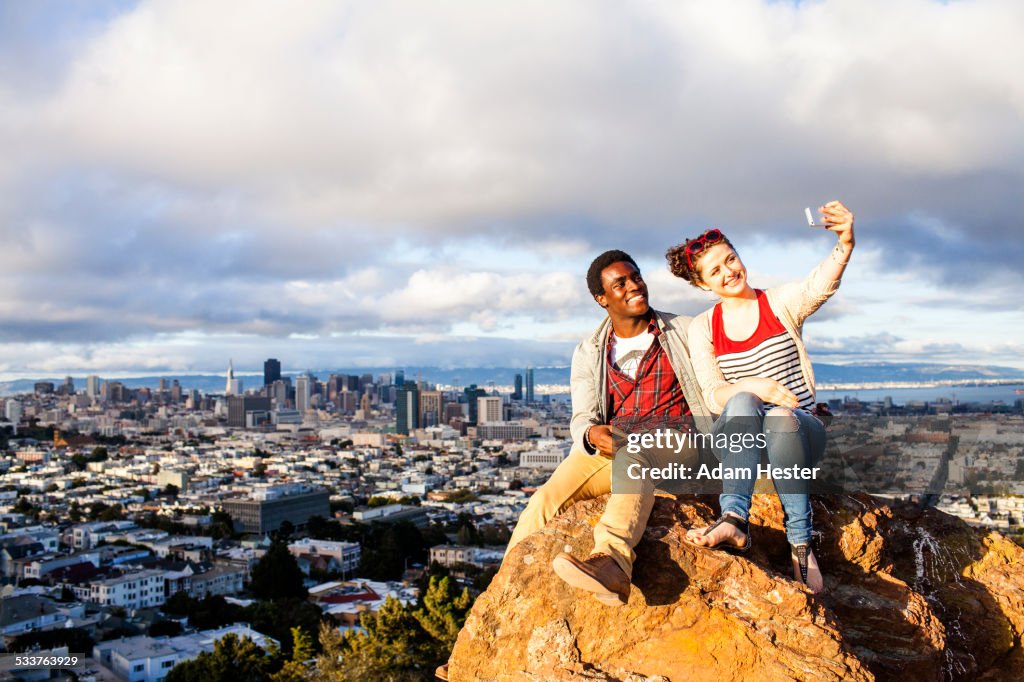 Couple taking cell phone selfie on rock overlooking cityscape