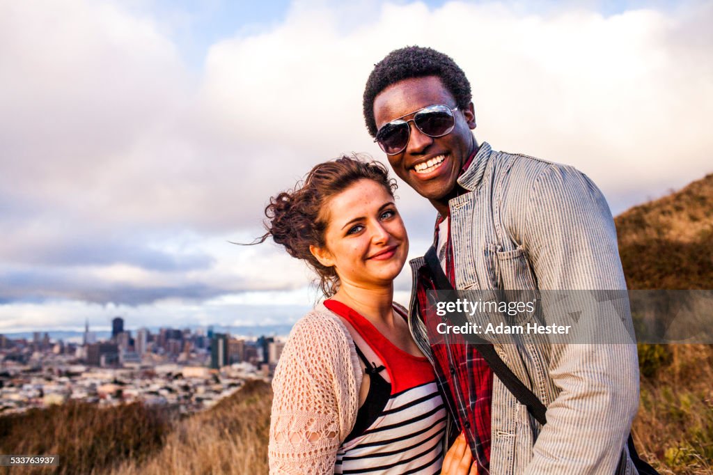 Couple smiling on grassy hill overlooking cityscape