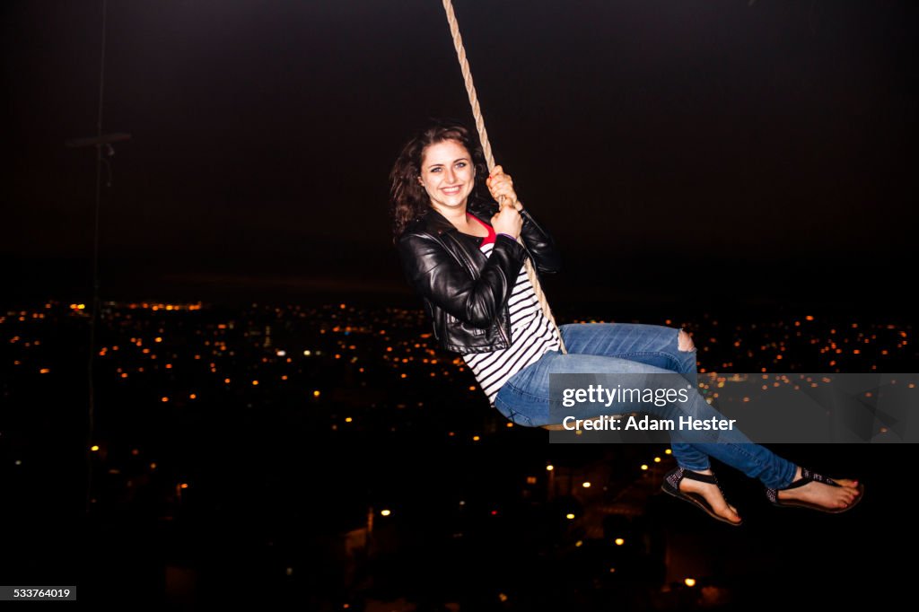 Caucasian woman on rope swinging over scenic view of cityscape