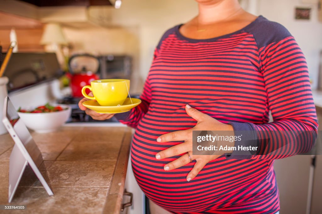 Pregnant Caucasian mother holding cup of tea in kitchen