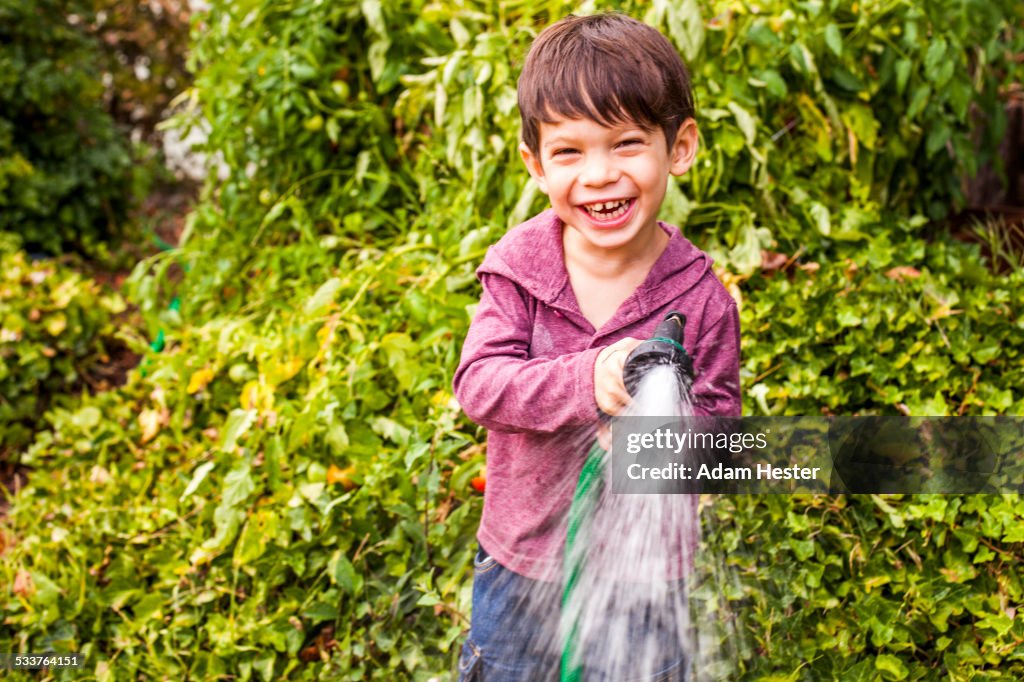 Mixed race boy playing with hose in garden