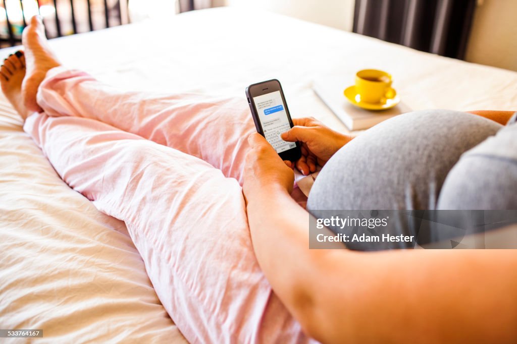 Pregnant Caucasian woman using cell phone in bed