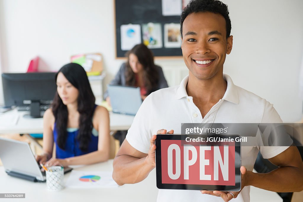 Businessman holding open sign on digital tablet in office
