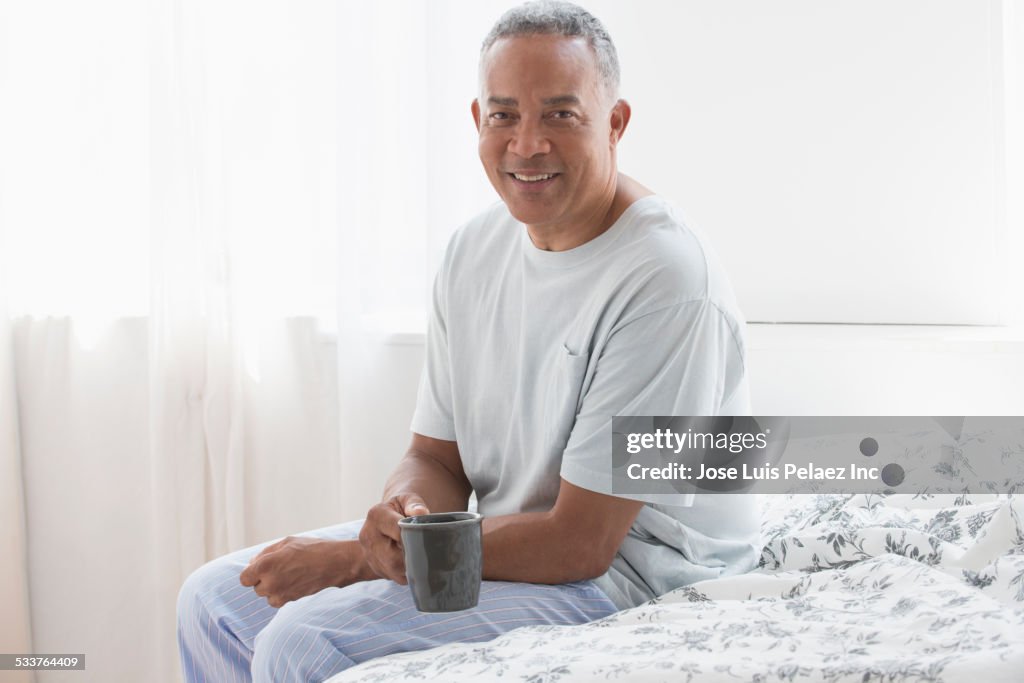 African American drinking cup of coffee on bed