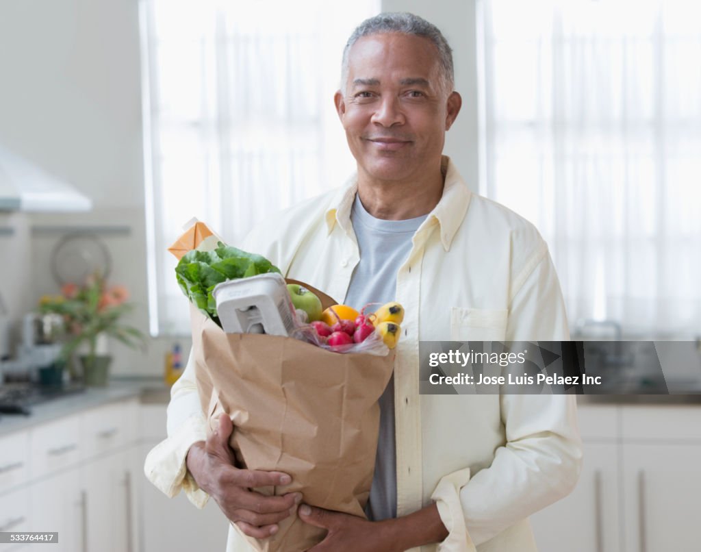 African American man carrying bag of groceries in kitchen