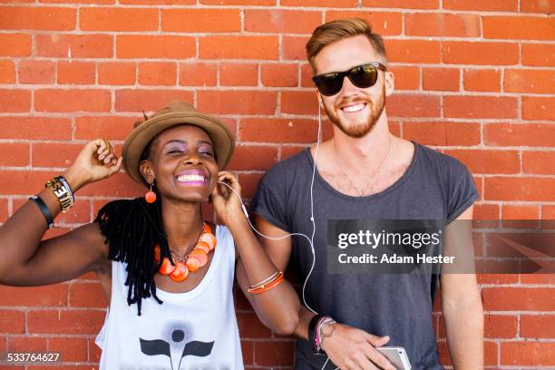 couple listening to earbuds near brick wall - freaky couples 個照片及圖片檔