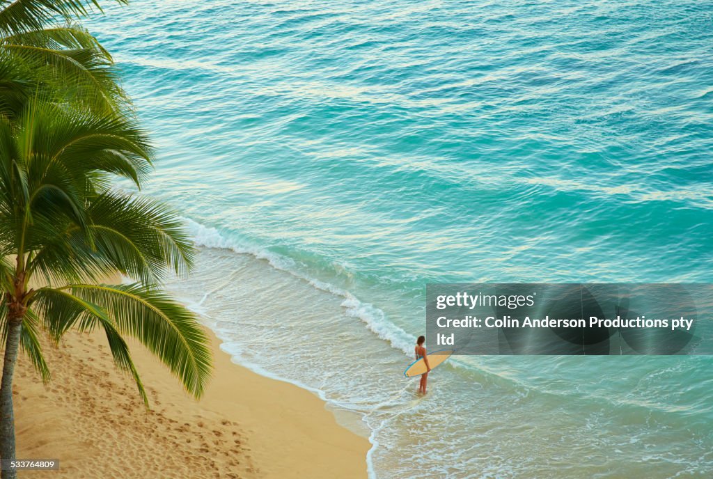 High angle view of Pacific Islander woman carrying surfboard on beach