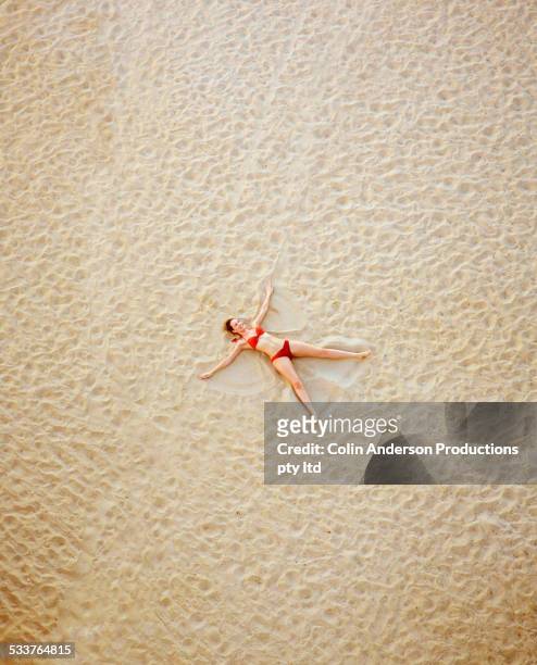 high angle view of pacific islander woman making sand angel on beach - angel hot stock-fotos und bilder