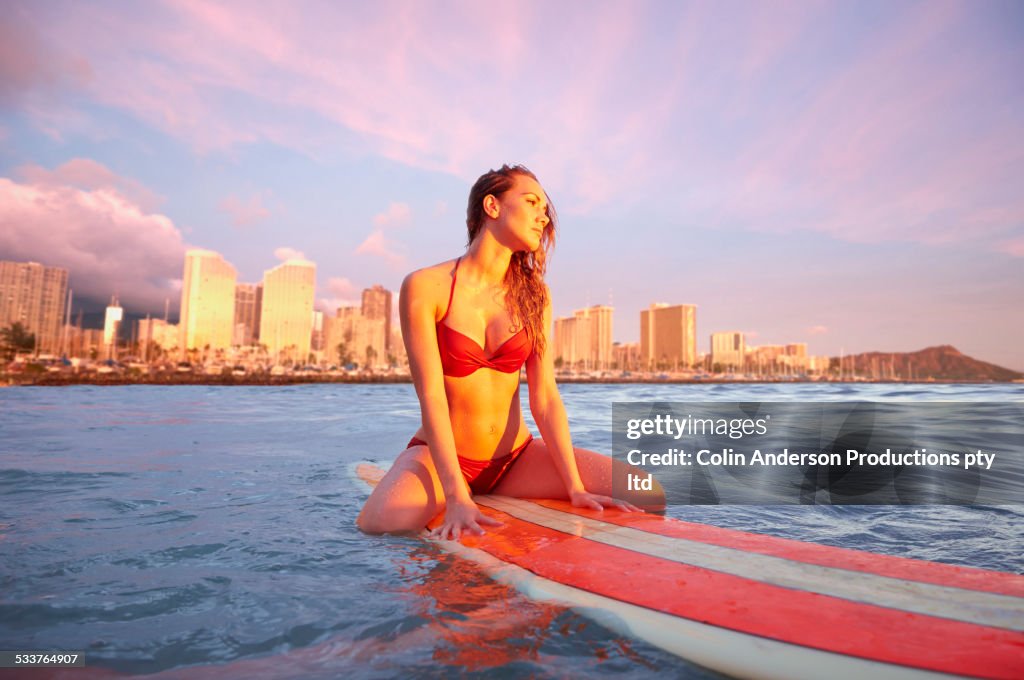 Pacific Islander woman floating on surfboard in ocean