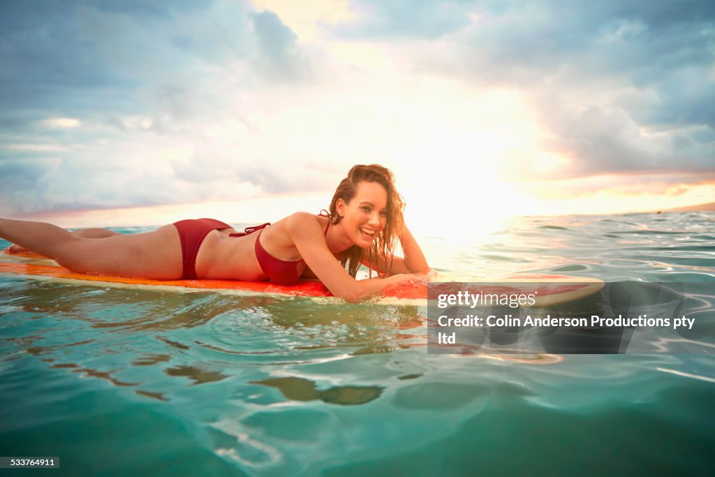 Pacific Islander woman floating on surfboard in ocean
