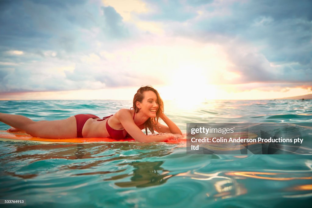 Pacific Islander woman floating on surfboard in ocean