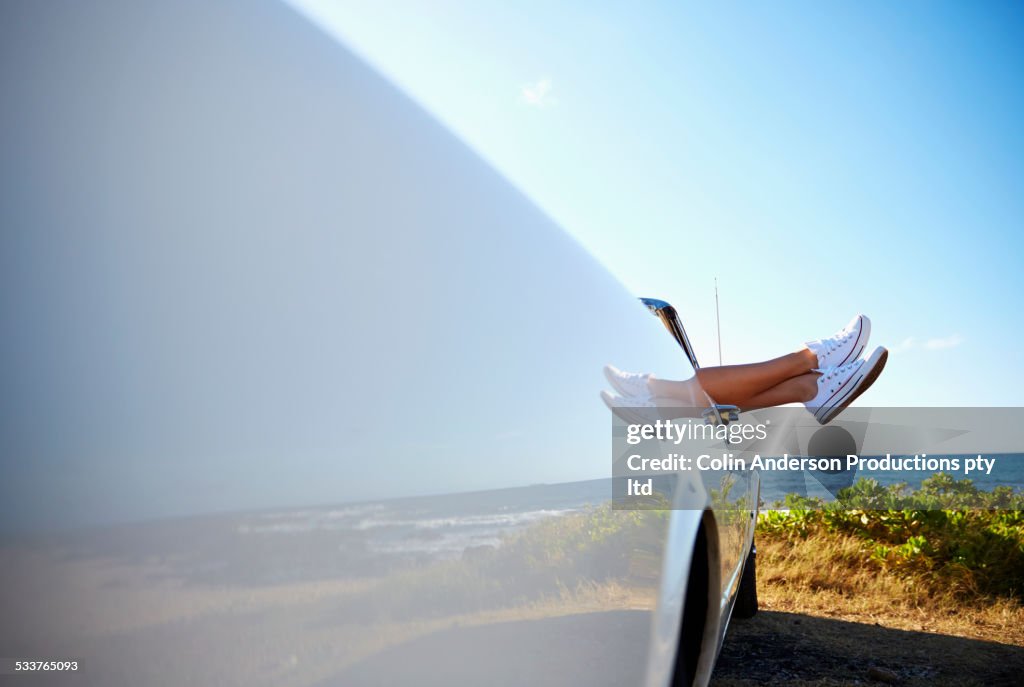 Feet of woman protruding from convertible on beach