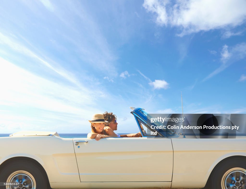 Caucasian couple driving convertible under blue sky
