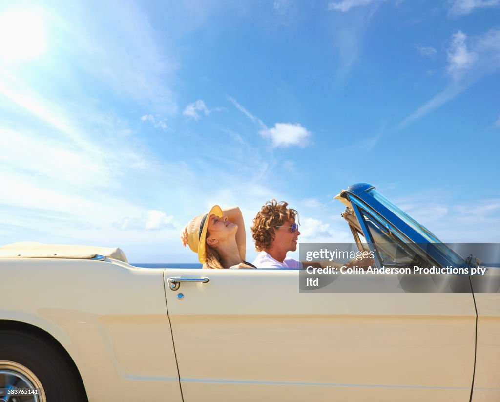 Caucasian couple driving convertible under blue sky