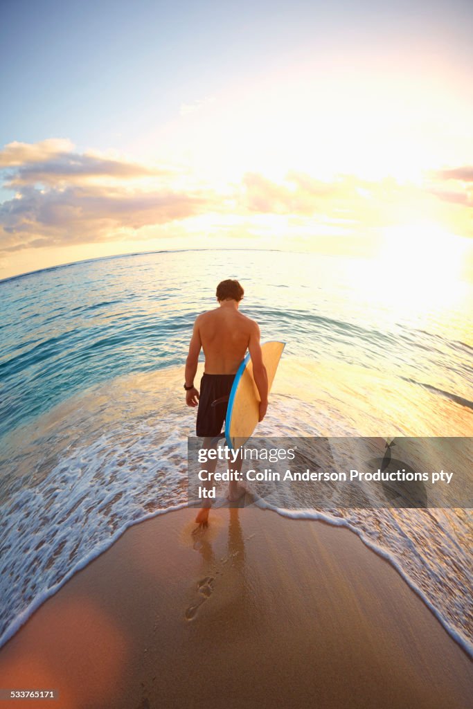 Caucasian teenage boy carrying surfboard on beach