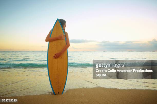 caucasian girl hugging surfboard on beach - beach hold surfboard stock-fotos und bilder