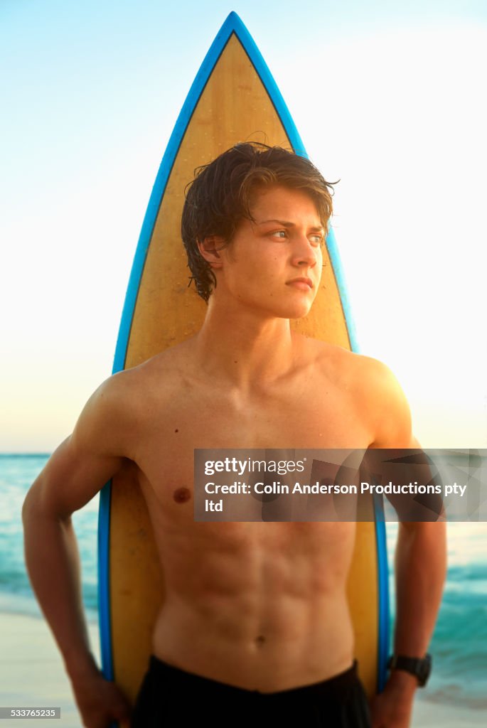 Caucasian teenage boy standing with surfboard on beach