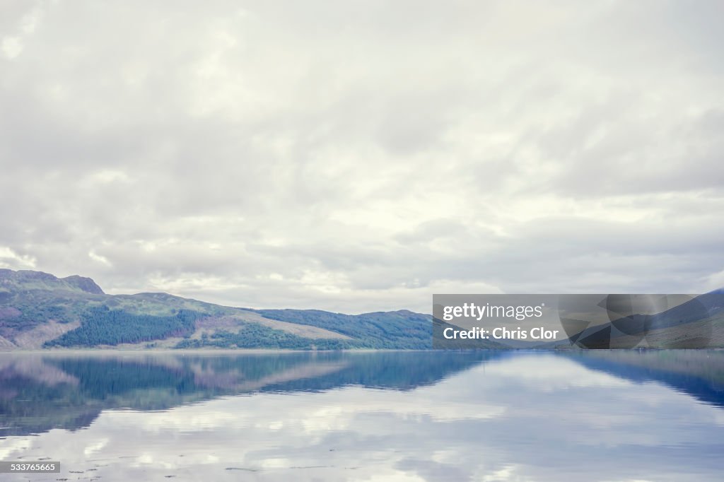 Cloudy sky and hilly landscape reflected in still lake