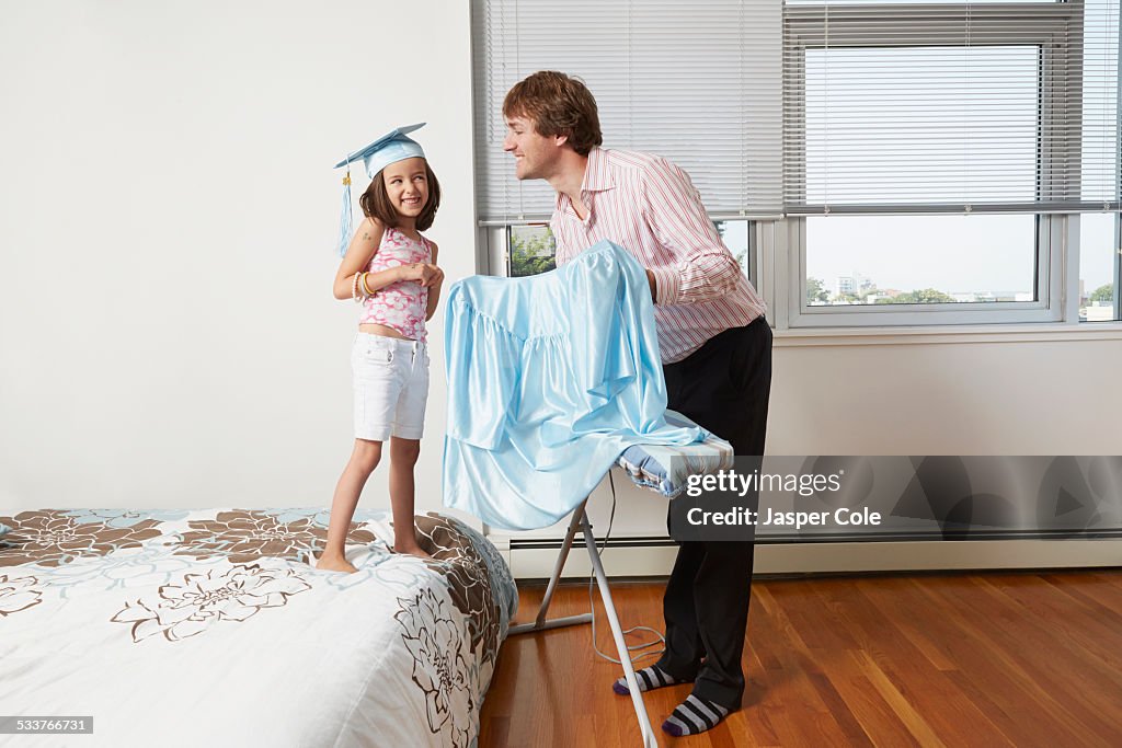 Father helping daughter with graduation robes