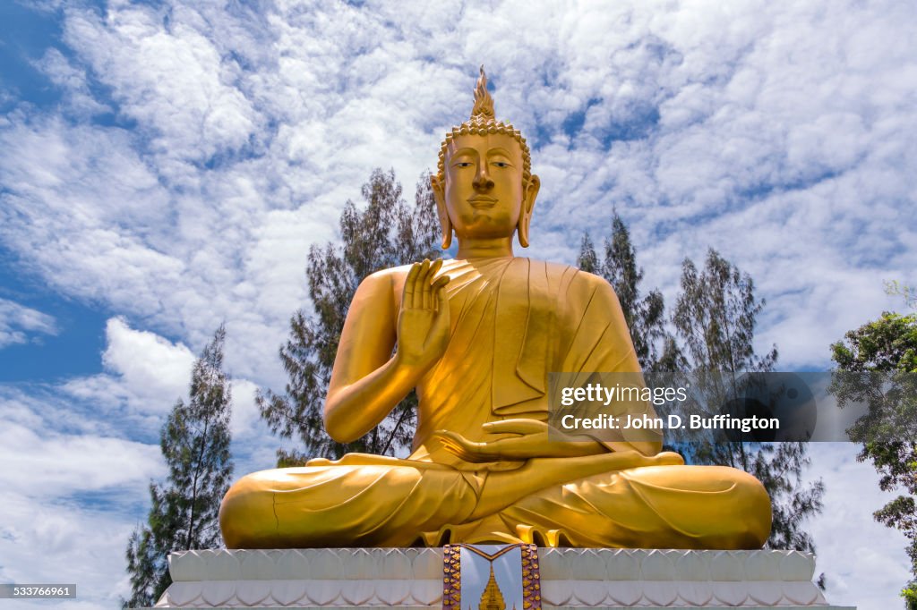 Low angle view of golden Buddha statue under cloudy sky