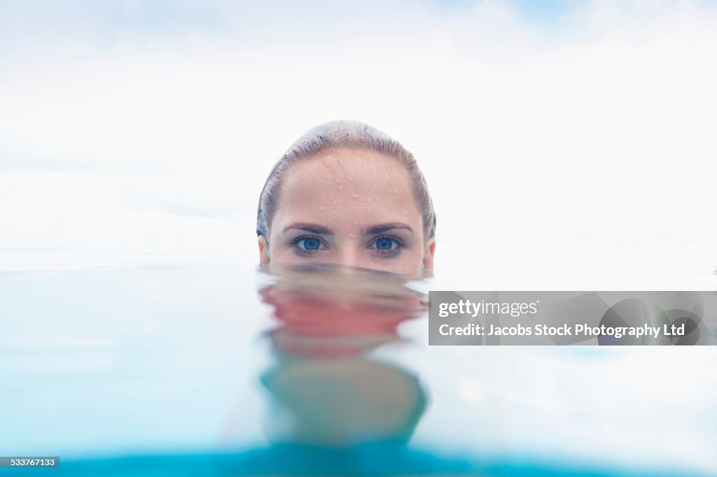 Caucasian woman peering over swimming pool water surface