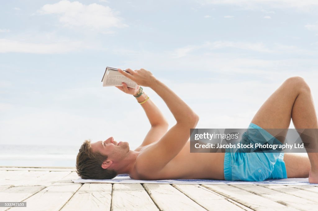 Caucasian man reading and sunbathing on wooden dock