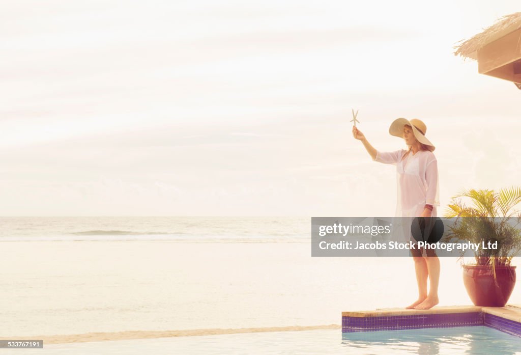 Caucasian woman holding starfish near swimming pool