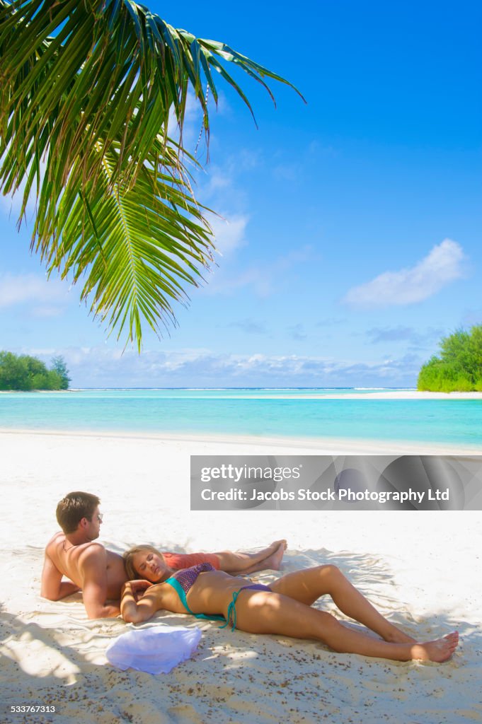 Caucasian couple relaxing in shade on tropical beach