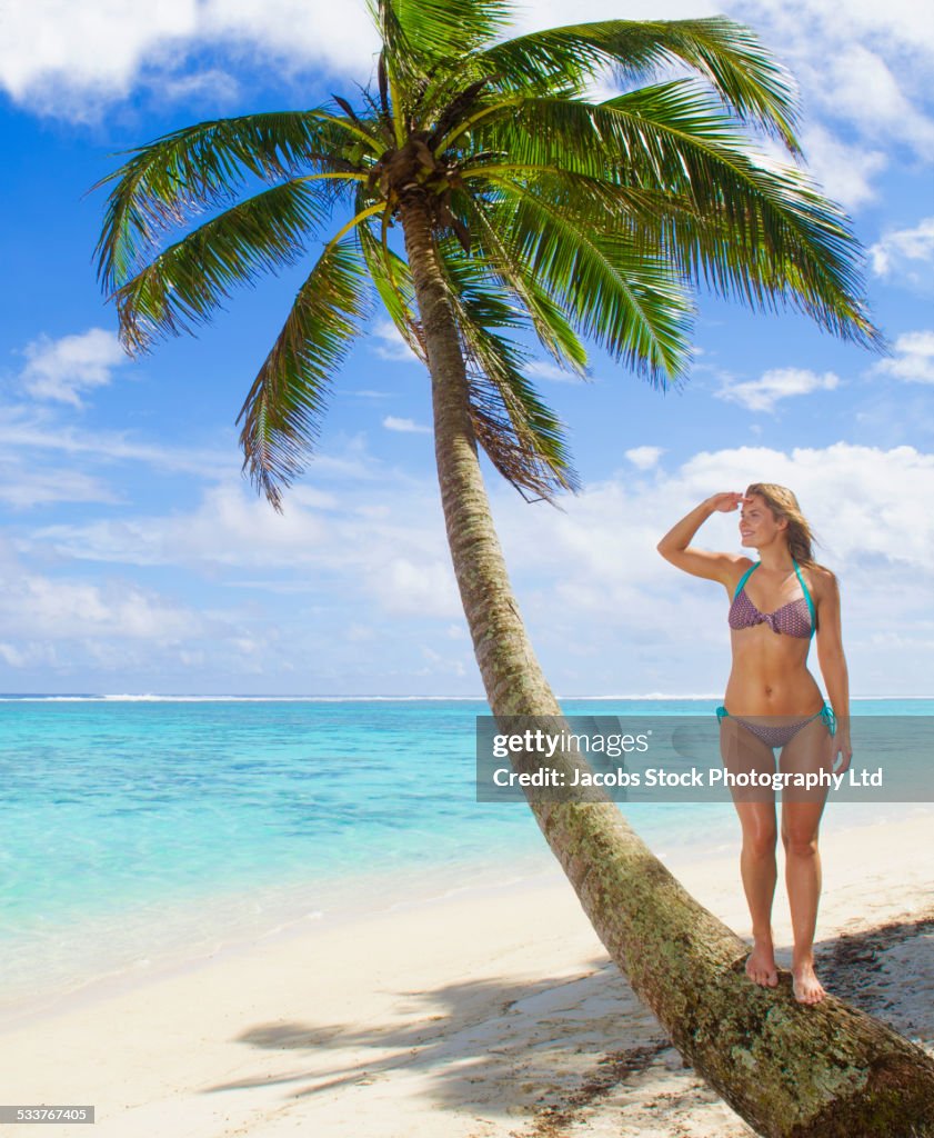 Caucasian woman standing on palm tree on tropical beach