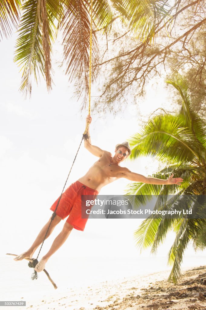 Caucasian man playing on rope swing on tropical beach