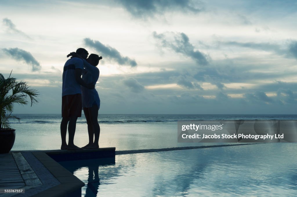 Caucasian couple kissing near swimming pool at sunset