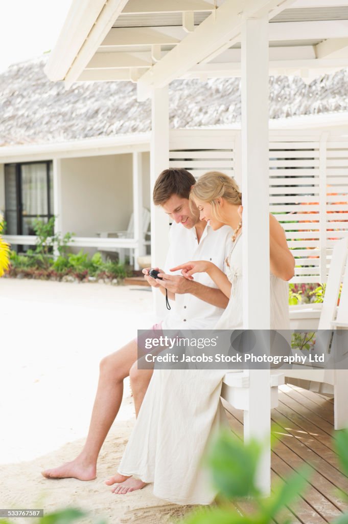 Caucasian couple examining photos on camera on porch railing