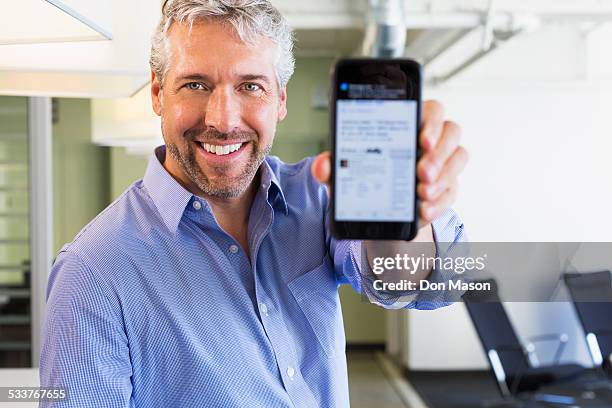 caucasian businessman holding cell phone in office - man showing phone photos et images de collection