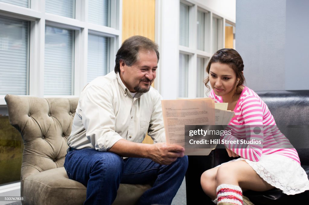 Hispanic teacher and student reading in campus lounge