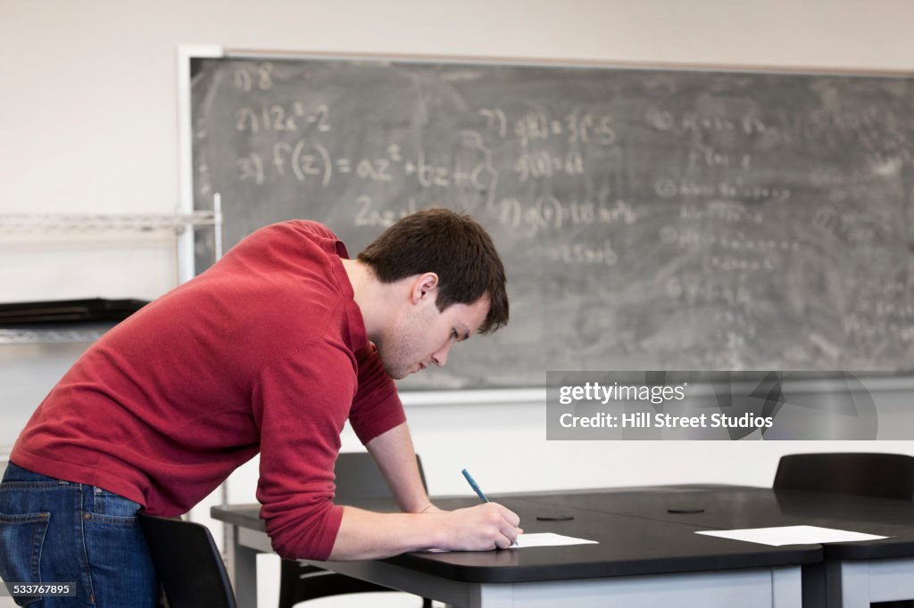 Caucasian student writing at table in classroom