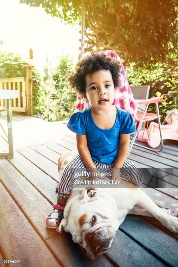 Mixed race girl sitting on dog on porch